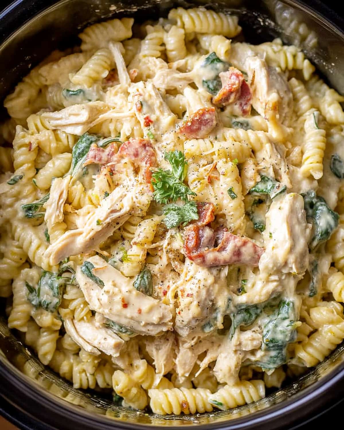 Crock Pot ranch chicken pasta with tender rotini, shredded chicken, crispy bacon, and spinach in a rich ranch-seasoned sauce.
