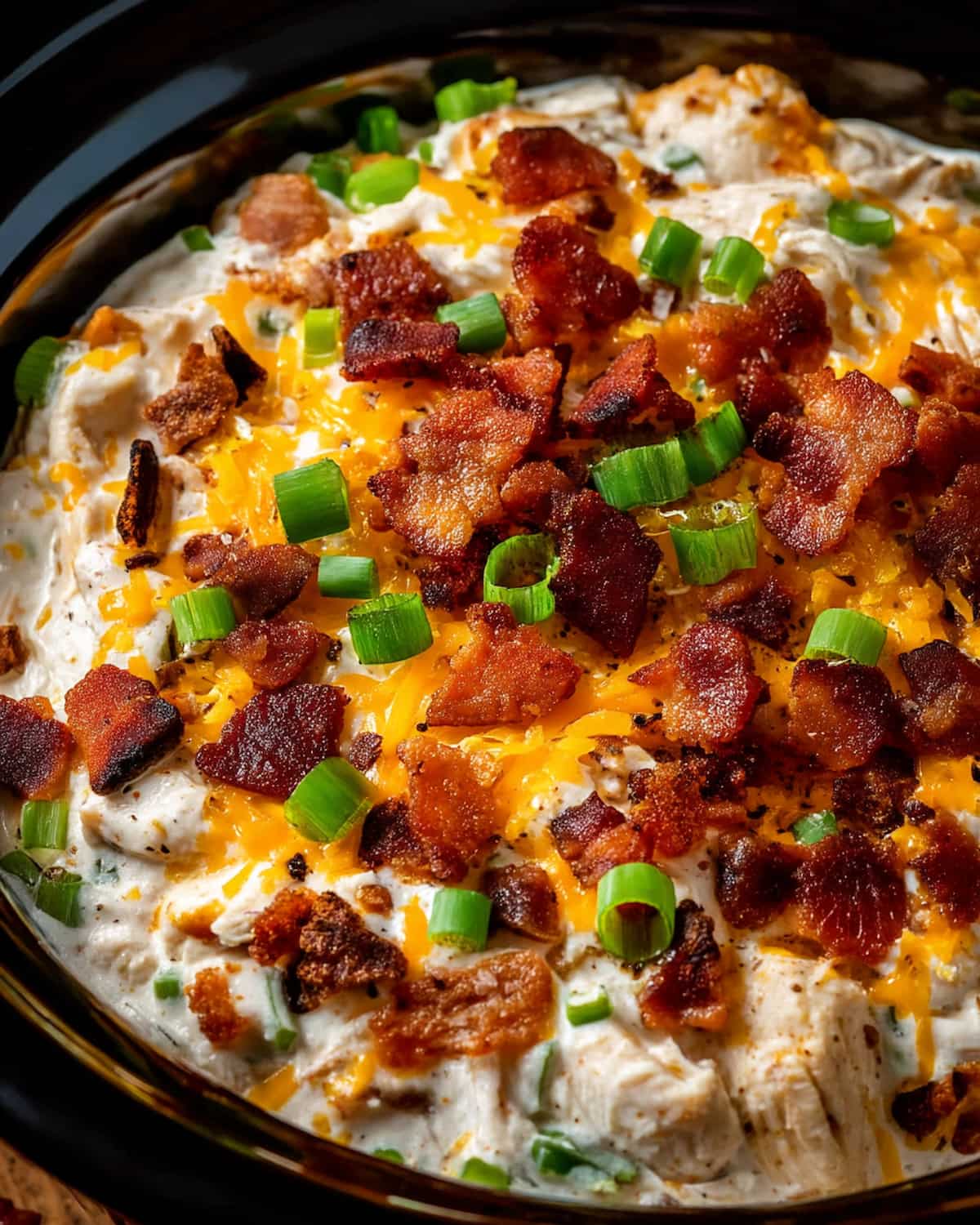 Crack chicken Crock Pot topped with crispy bacon, melted cheddar cheese, and chopped green onions.