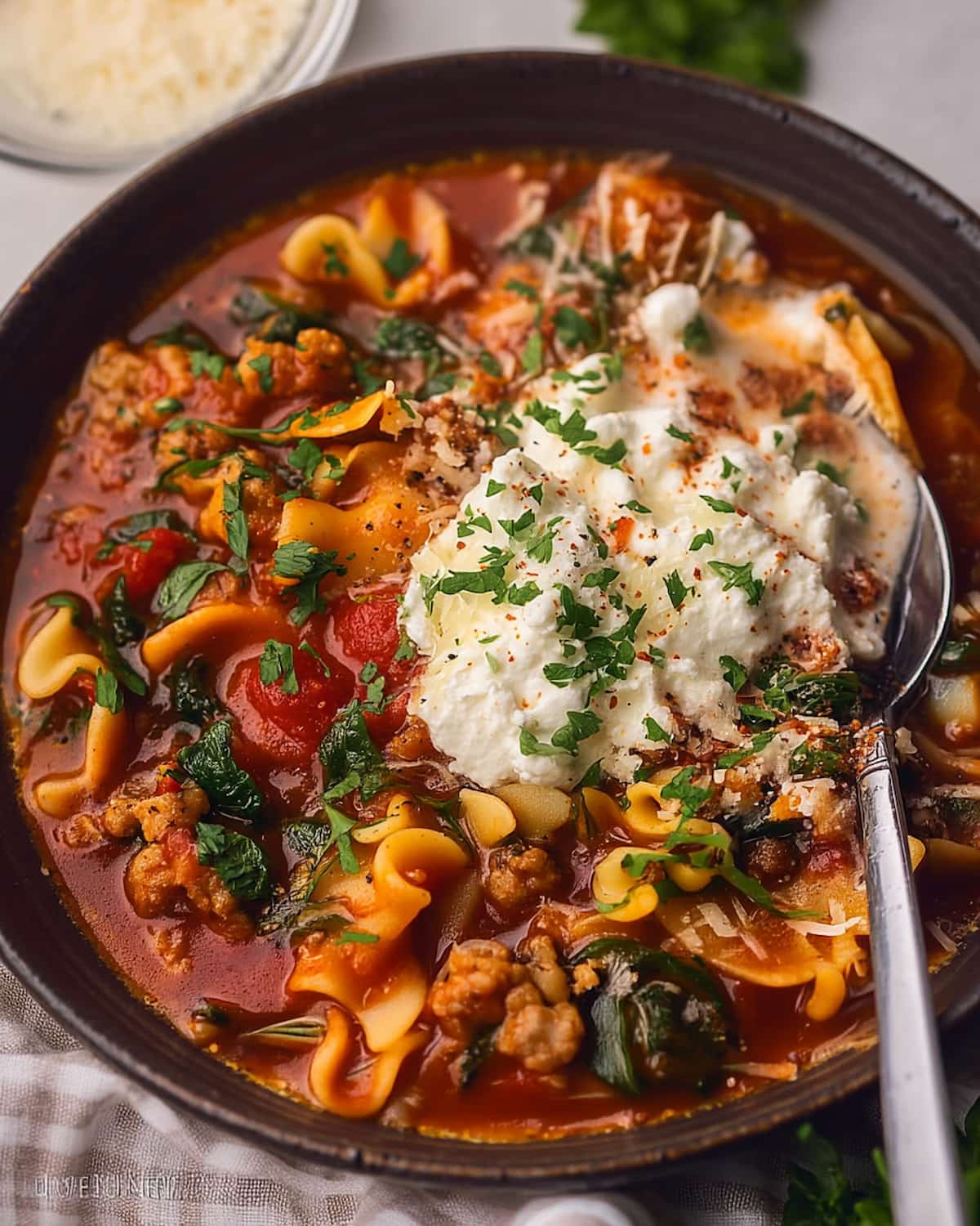 Lasagna soup Crock Pot filled with pasta, meat, and tomatoes, topped with a creamy cheese dollop.