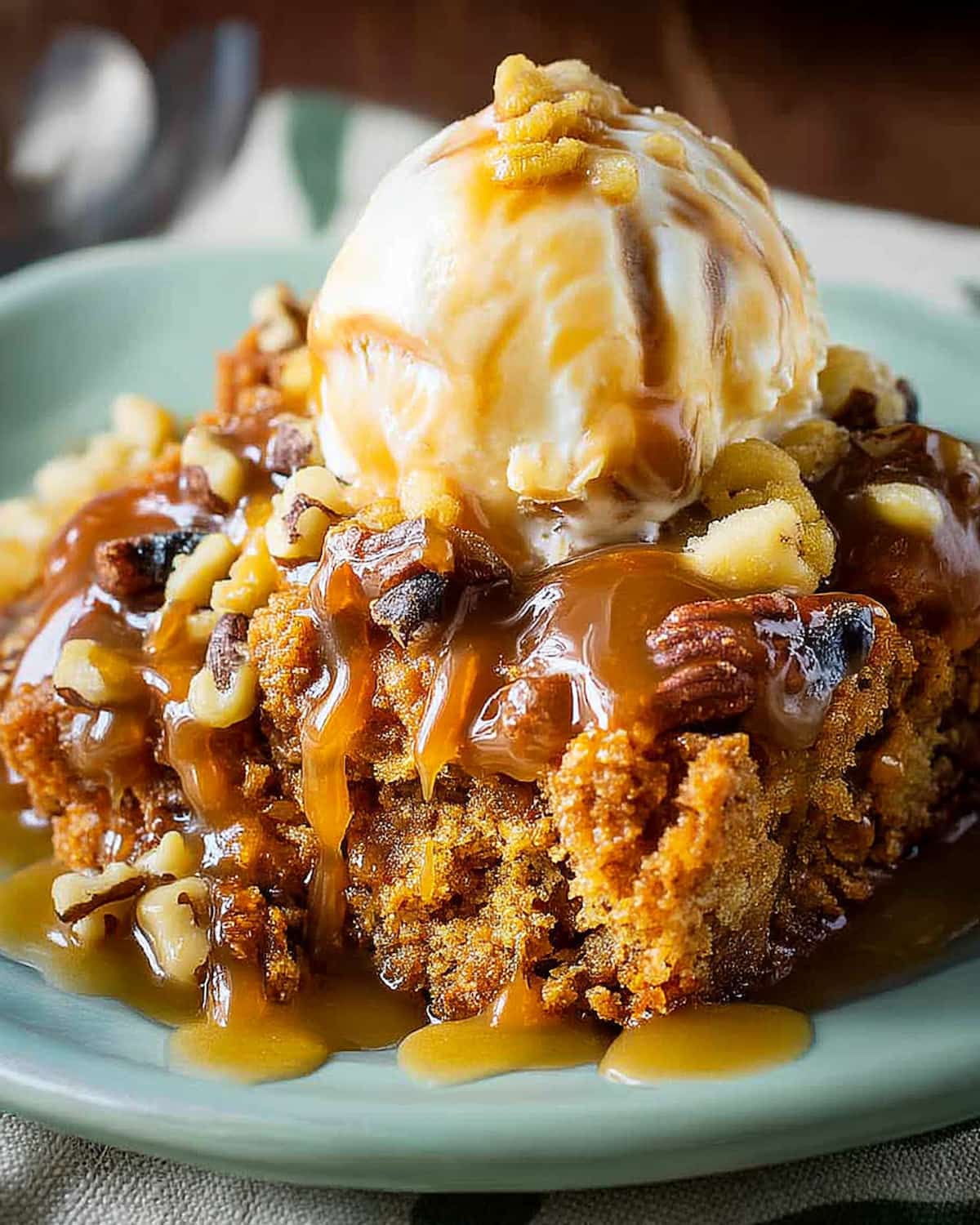 Slow Cooker pumpkin dump cake topped with vanilla ice cream, chopped nuts, and rich caramel sauce dripping.
