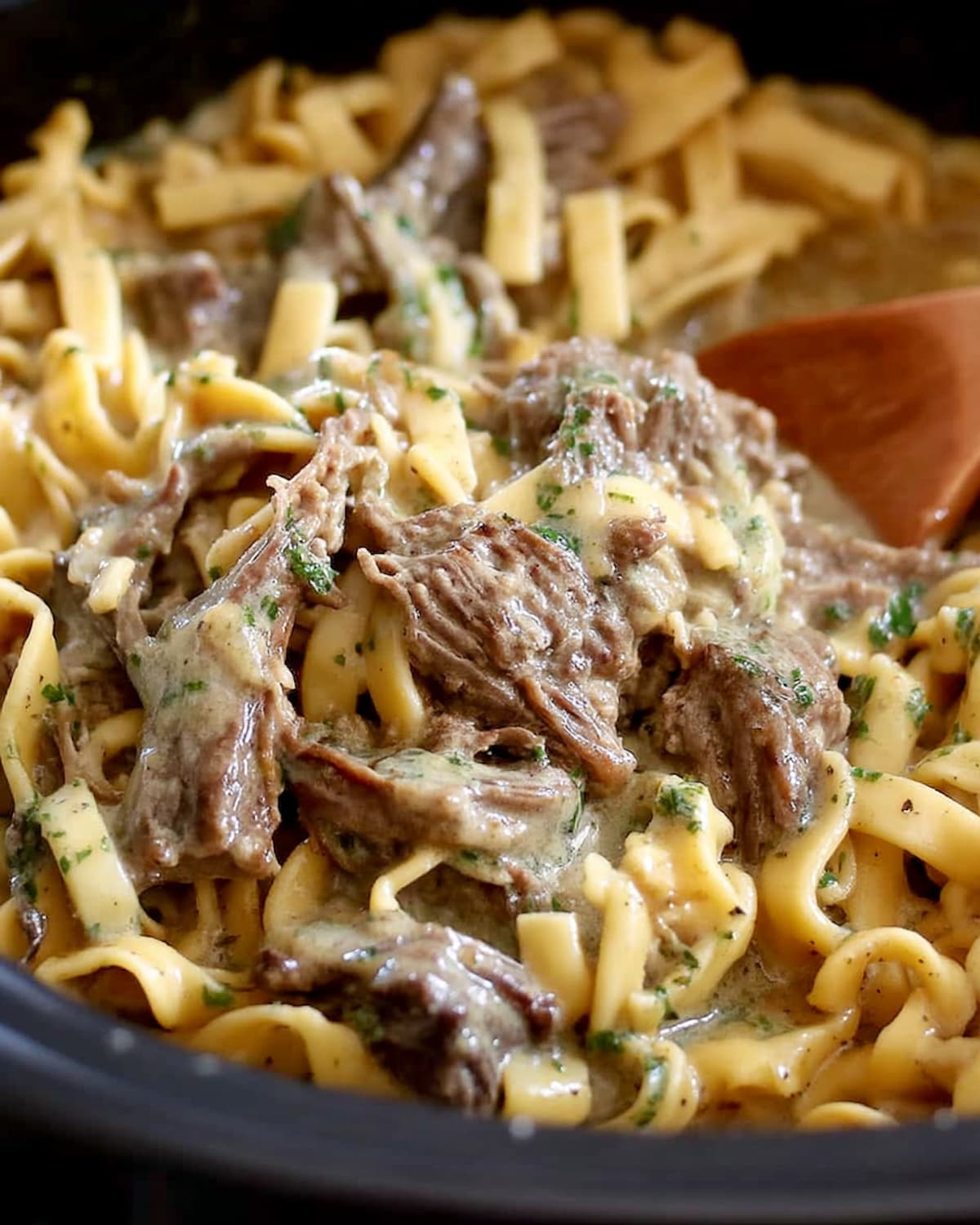 Bowl of Crock Pot beef tips and noodles with tender shredded beef in creamy sauce over egg noodles.