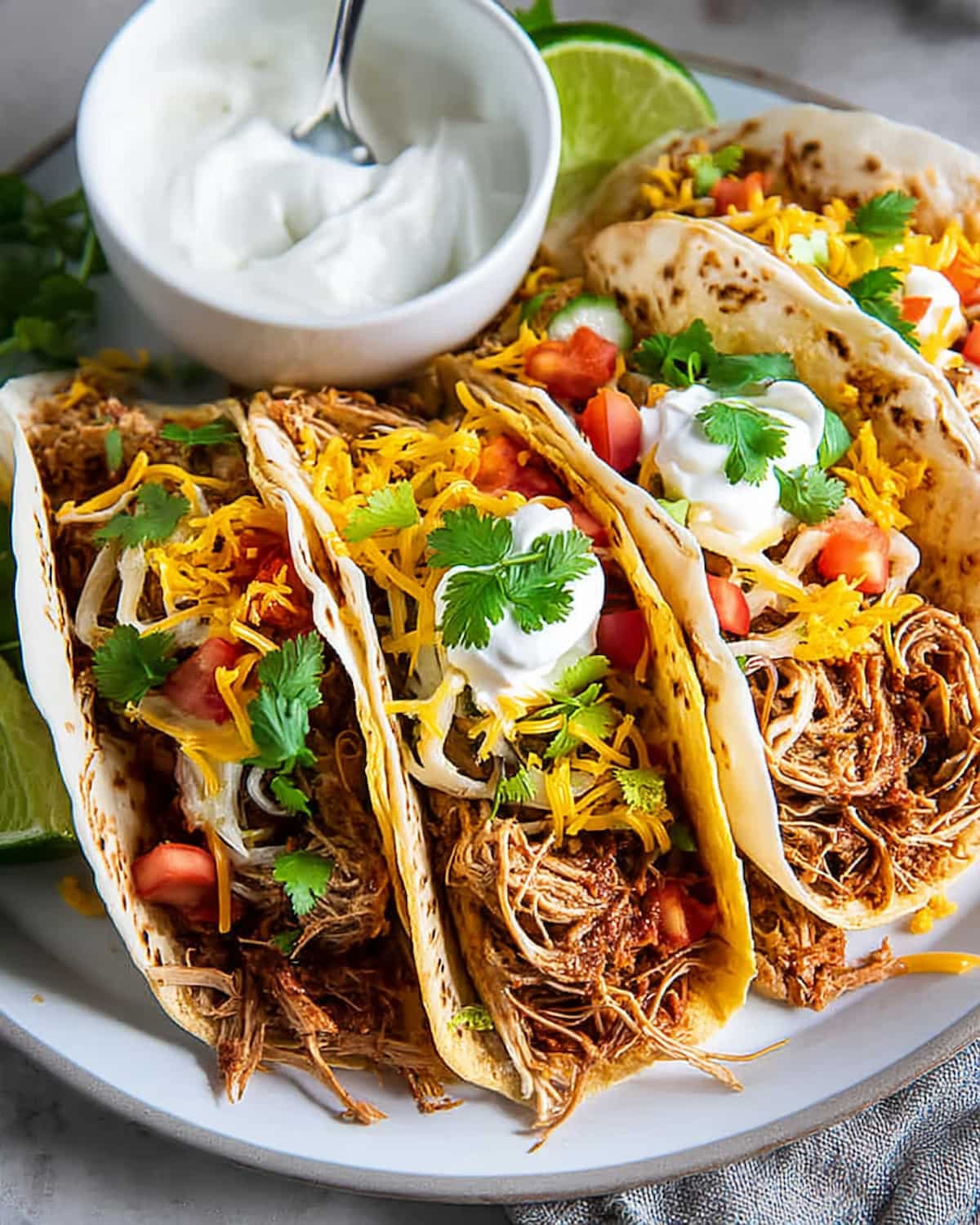 Crock Pot Chicken Tacos with shredded chicken, cheddar cheese, sour cream, diced tomatoes, and fresh cilantro.
