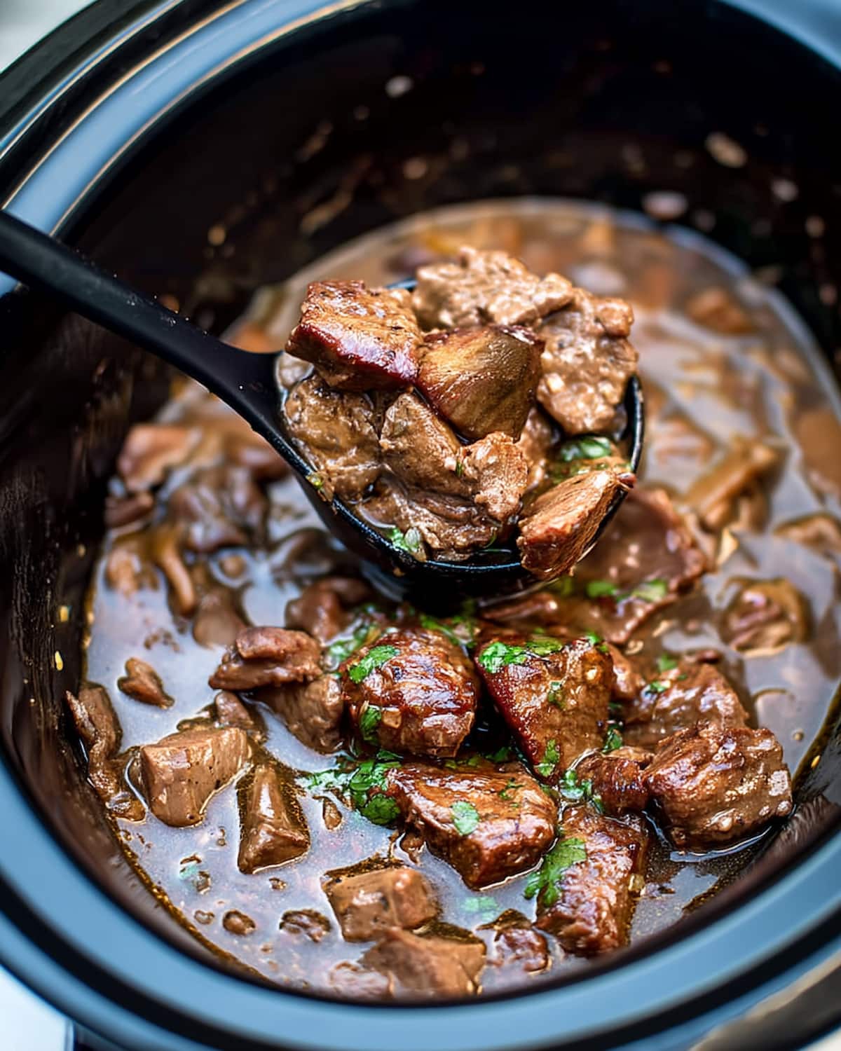 Sow cooker beef tips and gravy from a crock pot, showing tender browned beef chunks in rich brown gravy with parsley.