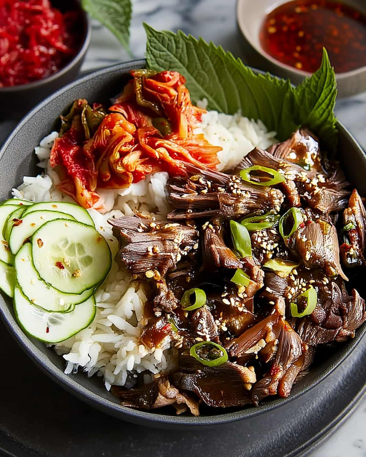 Slow Cooker Asian Short Ribs served over fluffy white rice, topped with sesame seeds and green onions, with cucumber slices and kimchi.