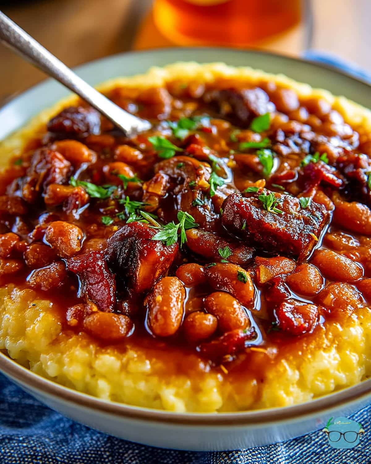 Crock Pot baked beans with smoky sauce, tender beans, and chunks of savory meat, served over creamy mashed cornmea.
