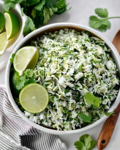 Slow Cooker cilantro lime rice garnished with fresh cilantro and lime wedges, served on striped napkin with wooden spoon.