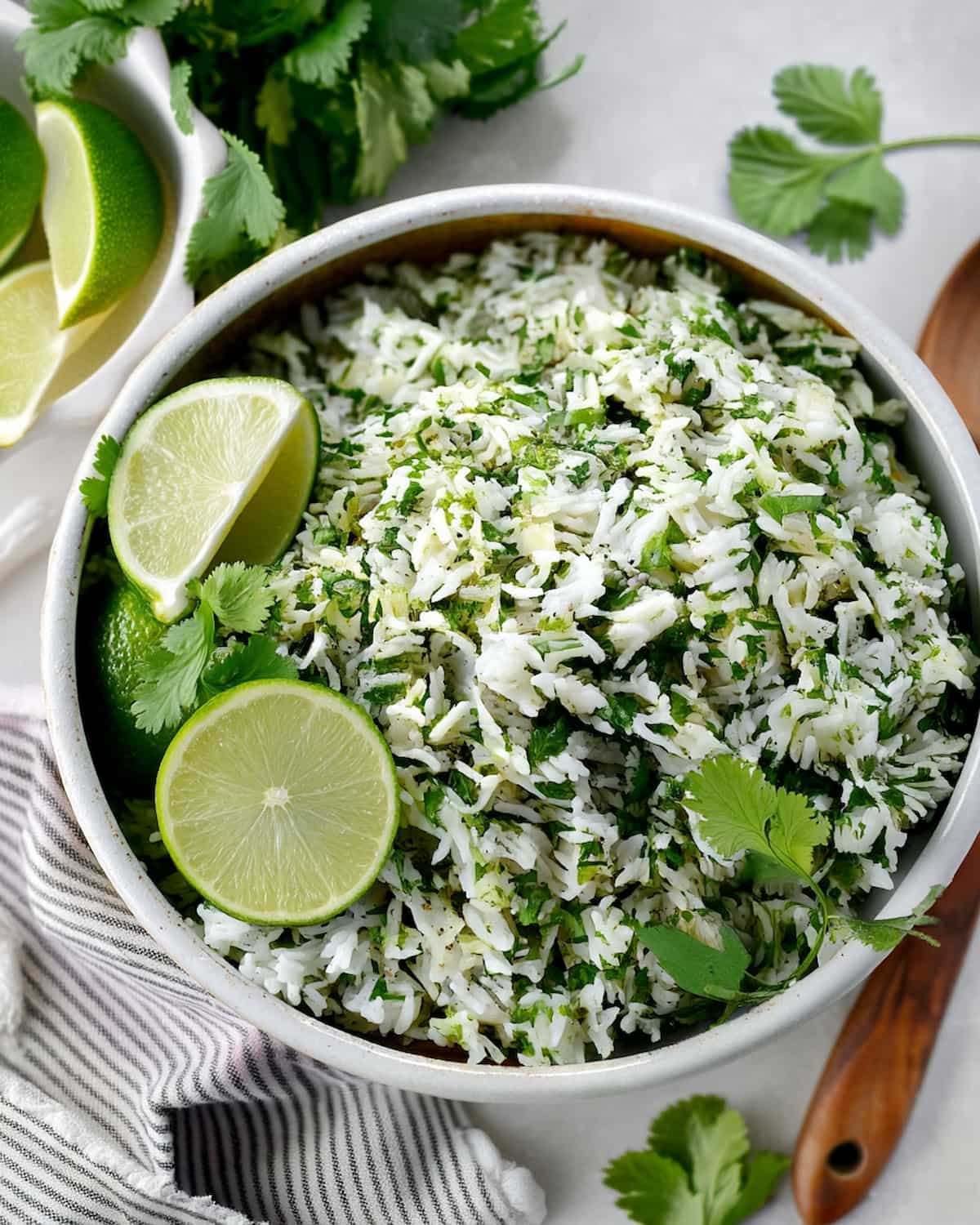 Slow Cooker cilantro lime rice garnished with fresh cilantro and lime wedges, served on striped napkin with wooden spoon.