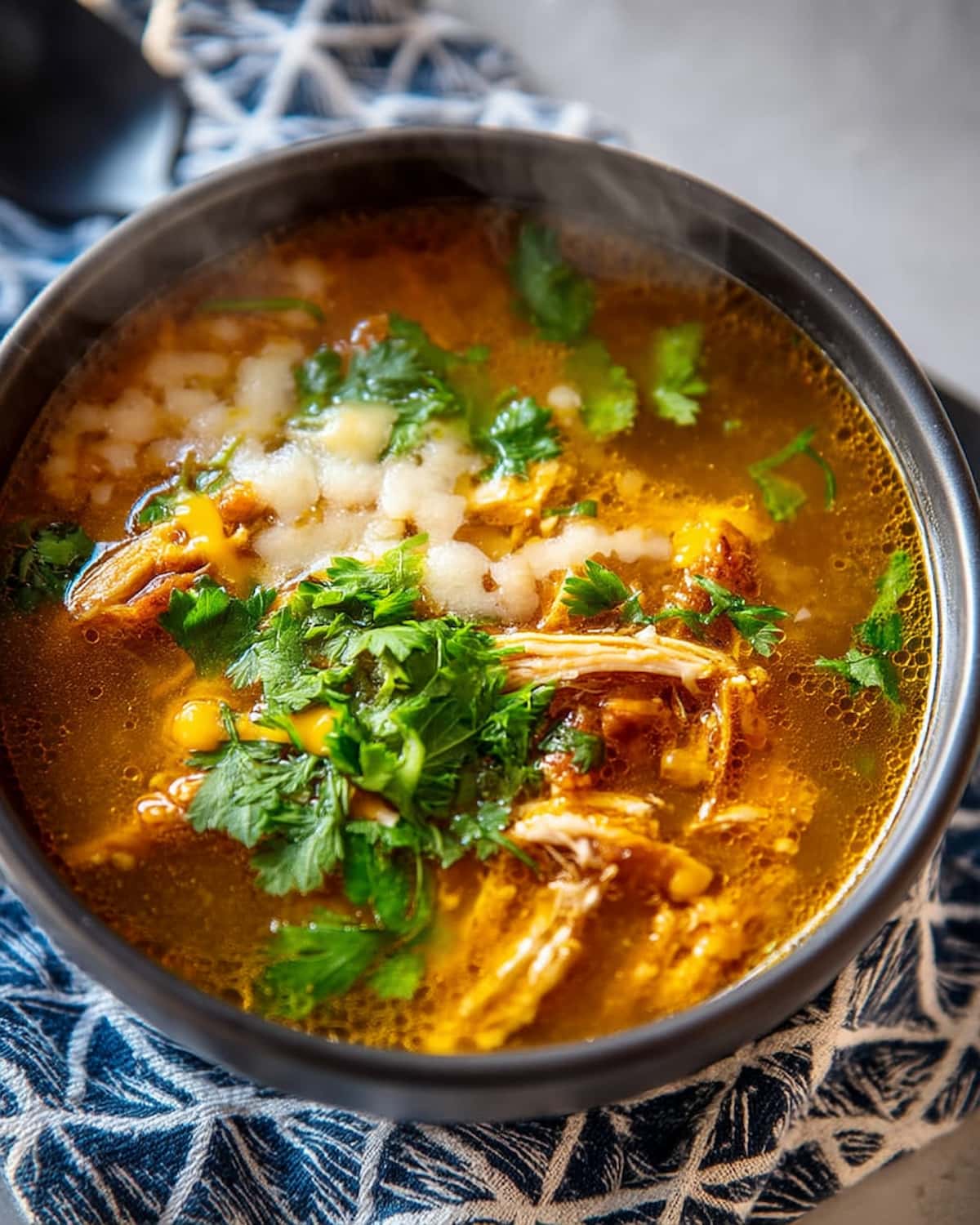 Slow Cooker green chicken chili with shredded chicken, golden broth, corn, white beans, and fresh cilantro on blue patterned cloth.