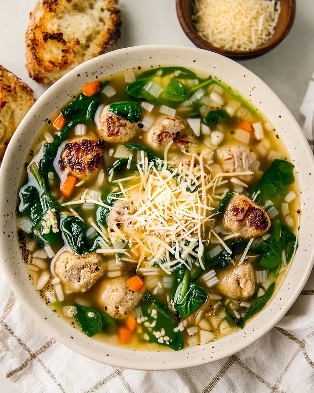 Slow Cooker italian wedding soup with tender meatballs, leafy greens, small pasta, and golden broth topped with grated cheese.