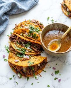Birria Tacos Crock Pot Recipe with crispy tortillas, shredded beef, melty cheese, and consommé for dipping