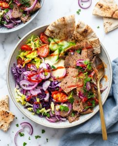 Slow Cooker Doner Kebab sliced thin with tender lamb, served with pita, salad, and creamy sauce on a plate